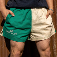 A person wearing rugby shorts that are bottle green on the top and cream on the bottom, with the brand name 'WOP-WOPS' embroidered on the front.