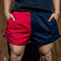 A person wearing a navy and pink harlequin-style rugby shorts with an elasticated waist and drawstring.
