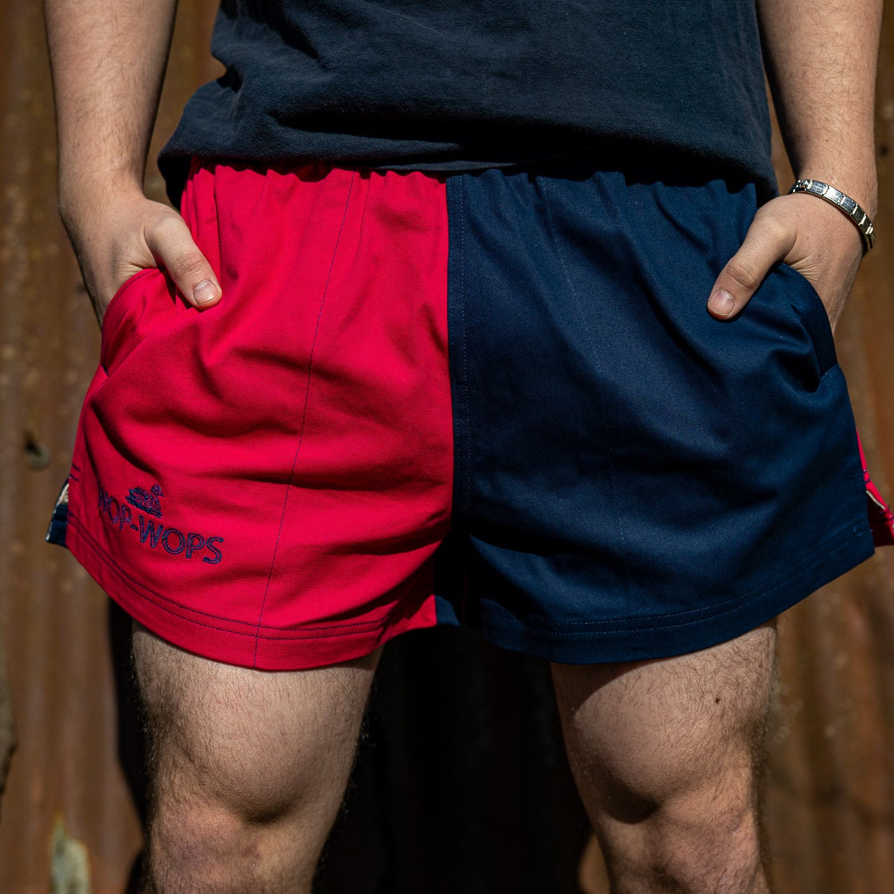 A person wearing a navy and pink harlequin-style rugby shorts with an elasticated waist and drawstring.