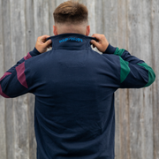 Person wearing a navy jacket with colorful sleeves, adjusting the collar against a wooden fence background.